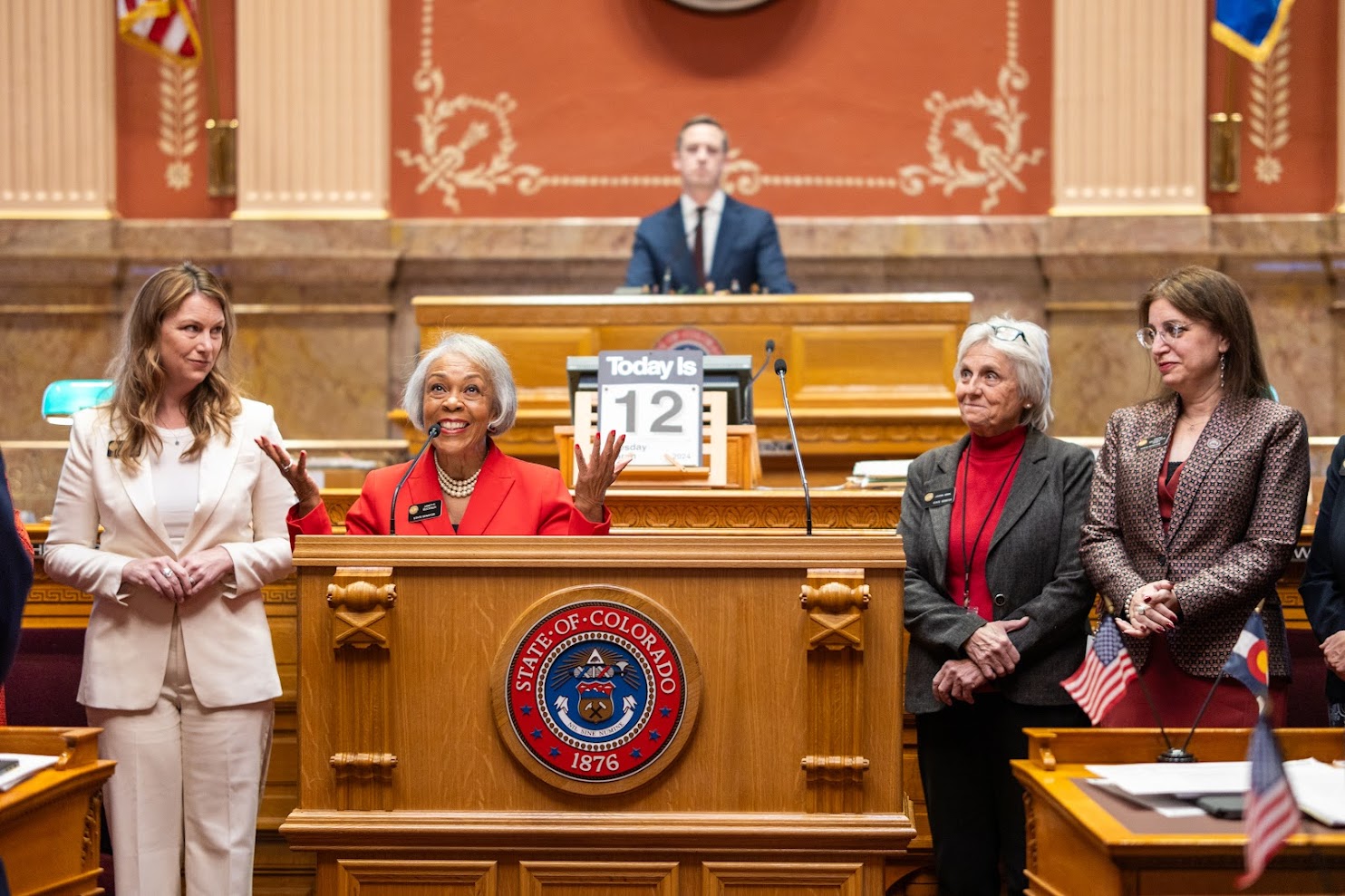 State Senator Janet Buckner addressing fellow legislators from the podium in the Colorado Senate chamber during a legislative session.