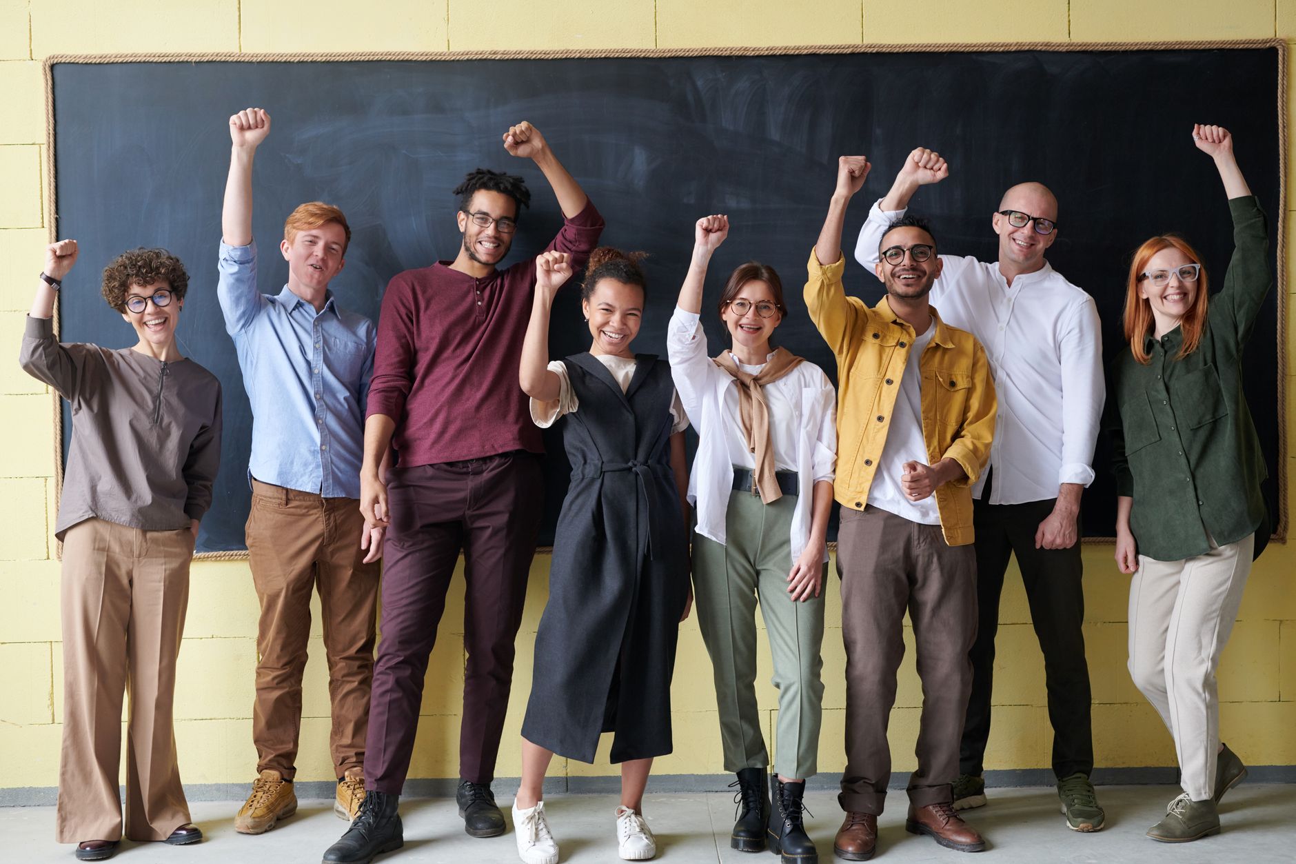 A diverse group of teachers standing together in a classroom with raised arms, symbolizing collaboration and support for education.