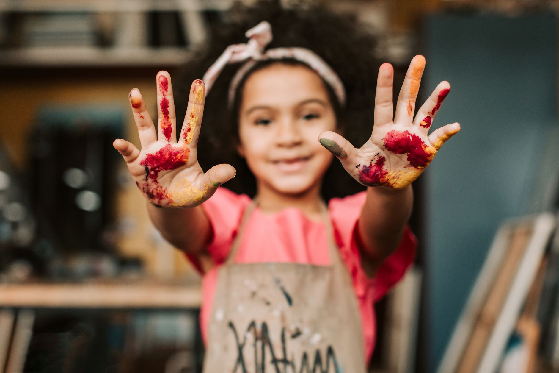 A young child with paint-covered hands held up toward the camera while participating in a creative art activity.
