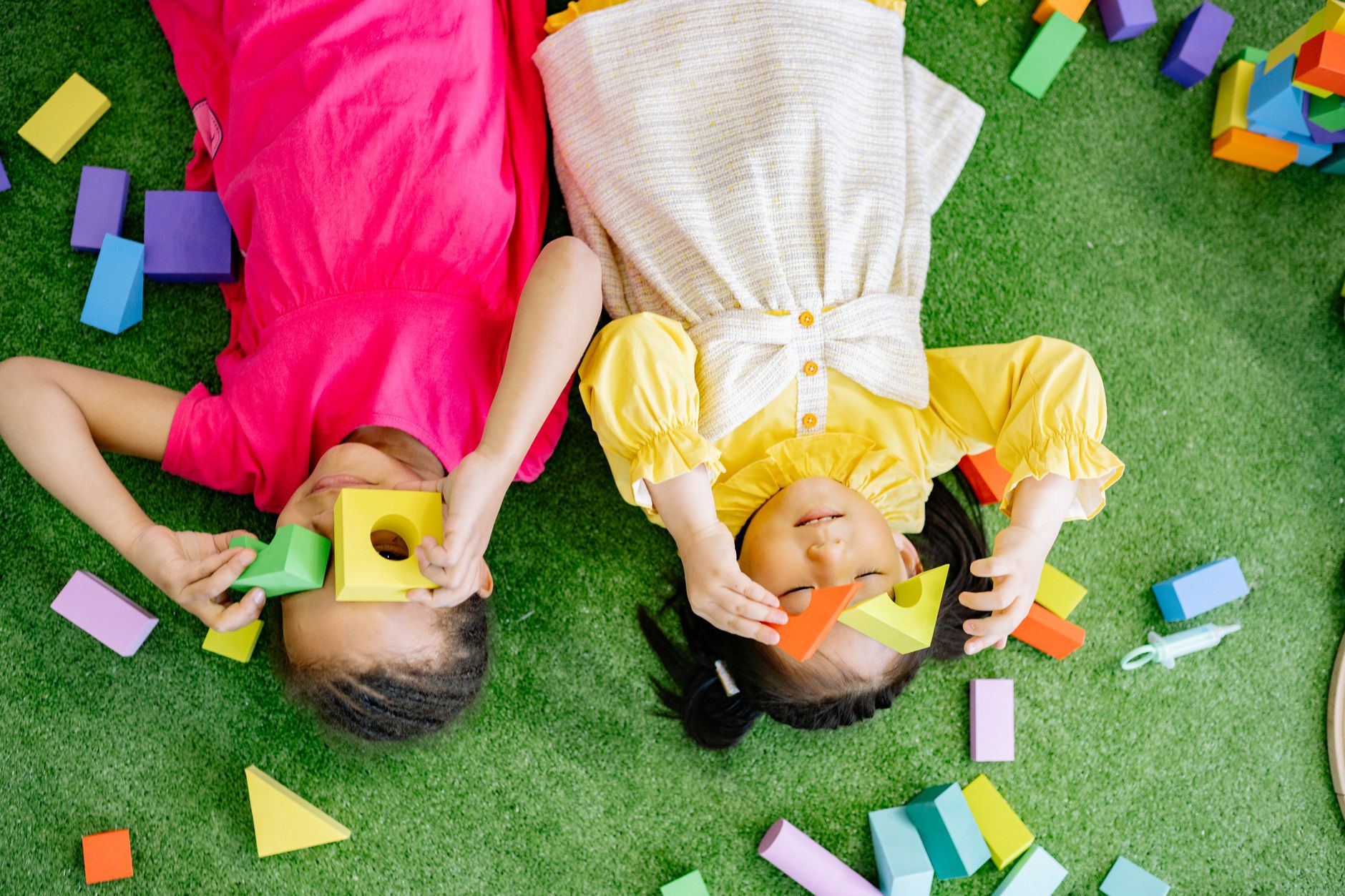 Two young children lying on a play surface and exploring colorful geometric blocks during a hands-on learning activity.