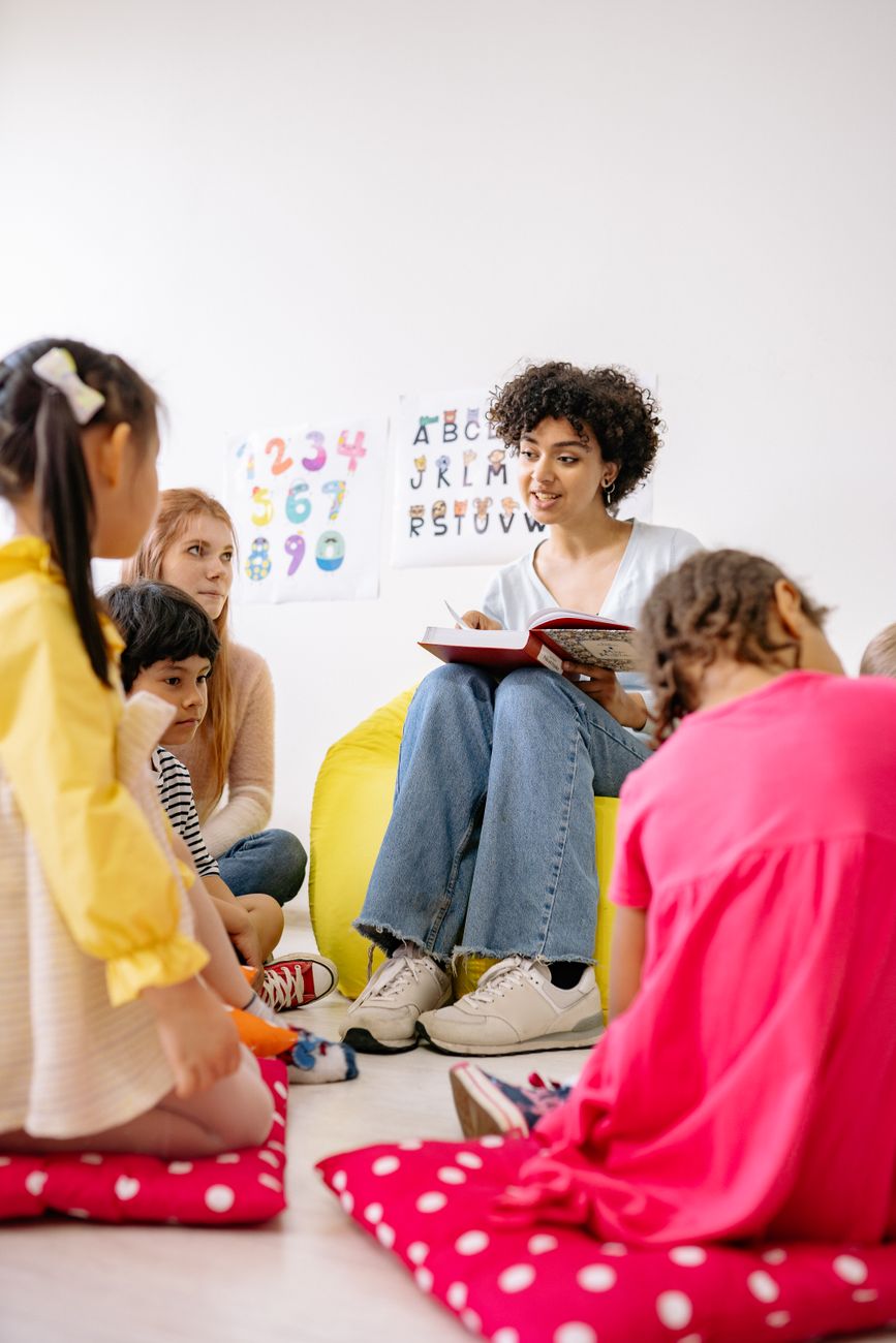 An early childhood educator reading with a small group of young children gathered in a classroom, supporting early learning and engagement.